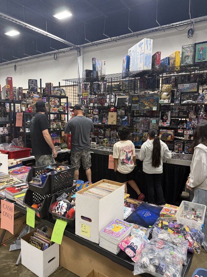 Kids and adults browsing comics, toys, and collectibles at a packed vendor booth