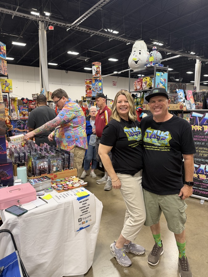 Smiling toy dealers standing in front of shelves packed with vintage toys and collectibles